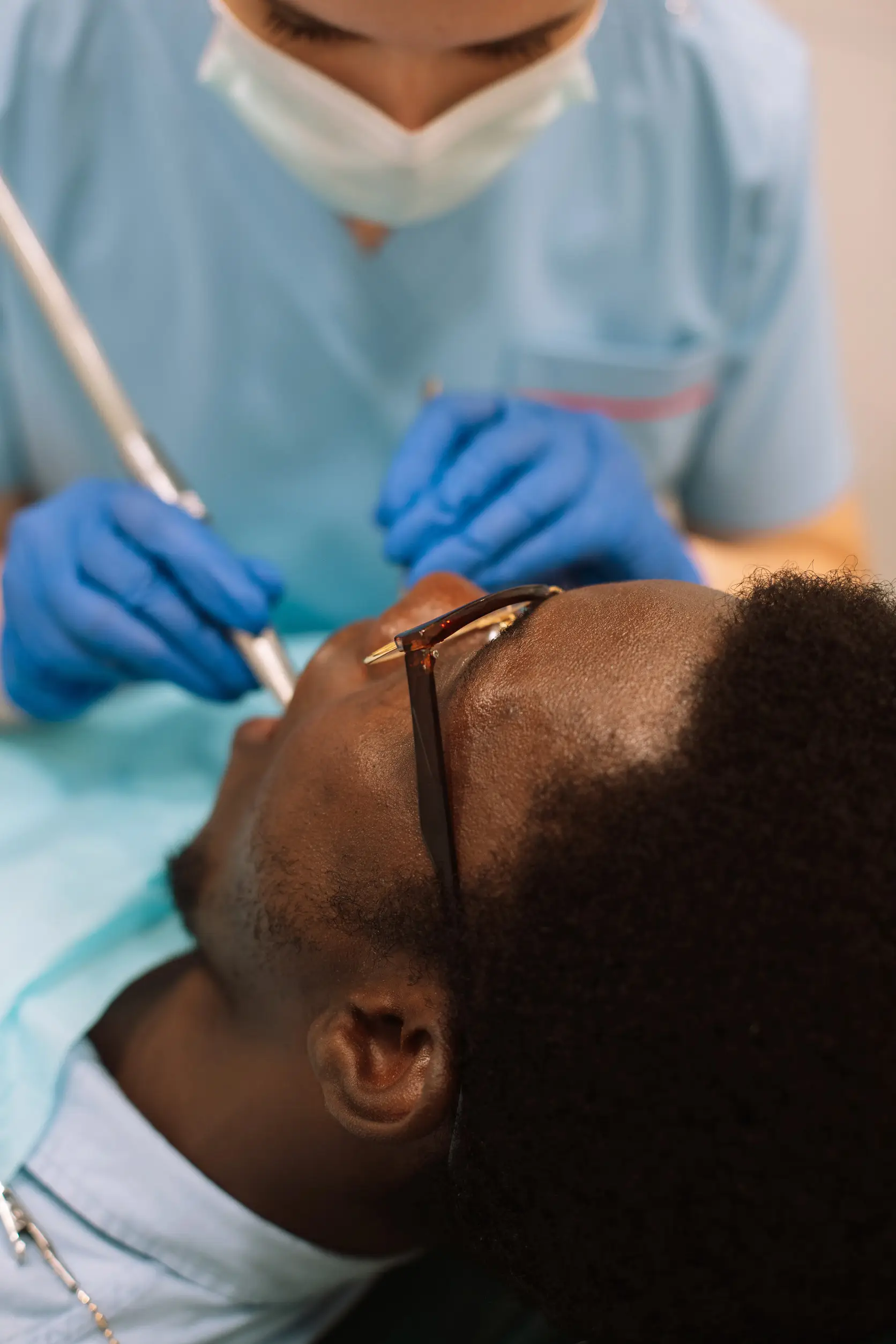 Portrait of black male patient getting teeth treatment with dentist at modern clinic, sitting in chair in white cabinet. professional stomatologist female using dental drill tool for young man.